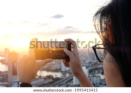 Asian woman take pictures of the buildings in the city. Sunrise time He uses a high-angle recording photo phone.Travel concepts and technology