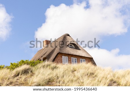a Sylt typical brick house with a thatched roof. shot of special red houses with meadow and grass in the foreground.  Royalty-Free Stock Photo #1995436640