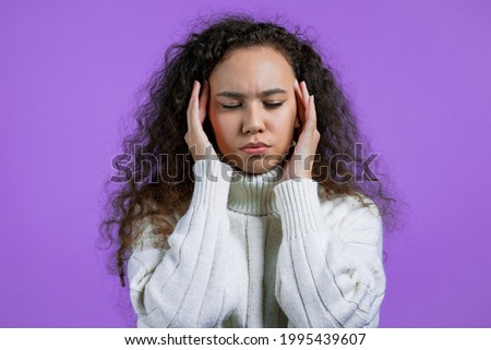 Portrait of woman having headache, purple studio portrait. Girl in winter sweater putting hands on head. Concept of migraine problems, medicine, illness