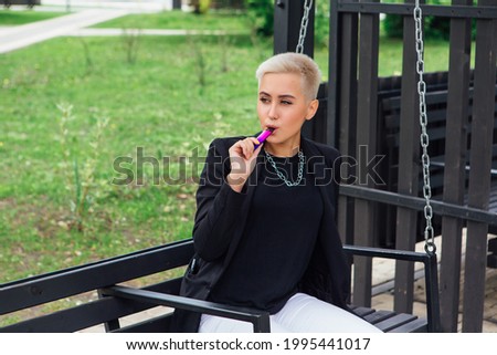Young stylish business woman with short hair and nose piercing. Confident girl look like lesbian sitting and smoking electronic cigarette on the swing