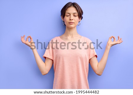 Calm caucasian female meditating with eyes closed isolated over purple background, engaged in yoga, keep calm, namaste. portrait of woman in casual clothes