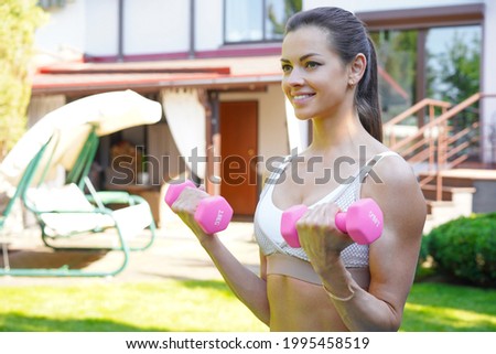 Young beautiful sports girl in leggings and a top does exercises with dumbbells. Healthy lifestyle. A woman goes in for sports outdoor at home