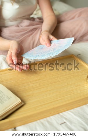 Female hands are holding cards. The girl makes a layout of metaphoric cards. Photo taken with selective focus and noise effect
