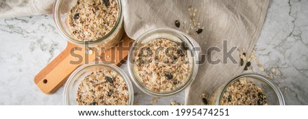 Raw dough of wholegrain bread with chia, oats, flaxseeds, sunflower and pumpkin seeds in glass jar for canning and prepper long term pantry on wooden board, linen towel and light marble background