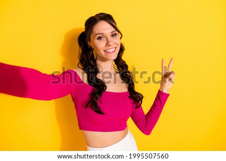 Photo of young cheerful girl happy positive smile make selfie show peace cool v-sign isolated over yellow color background