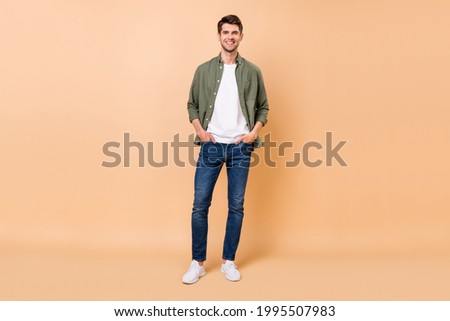 Full body photo of charming cheerful positive young man hold hands pockets isolated on beige color background Royalty-Free Stock Photo #1995507983