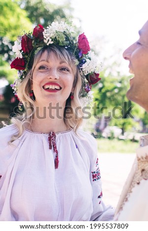 Young people are posing in traditional folk costumes. Cossacks man and woman in wreaths and embroidered shirts. Reconstruction of vintage traditions and customs. Guy and girl kiss