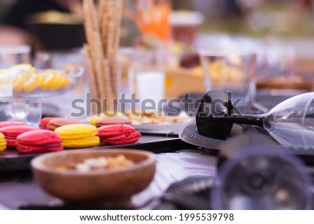 Close-up photo of colorful French macaroons on a feast table outside during summer with wine glasses and other snacks around 