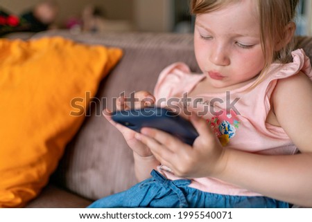 girl with blond hair plays with a smartphone at home. child and smartphone in hands. children with digital tablet