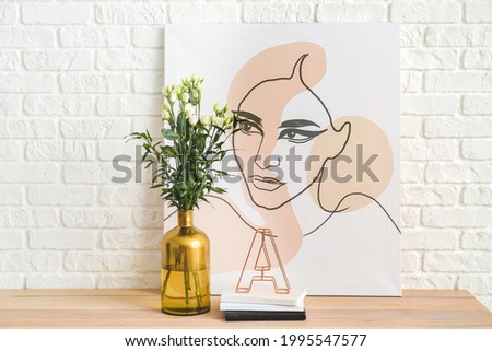 Vase with beautiful flowers, books and picture near white brick wall
