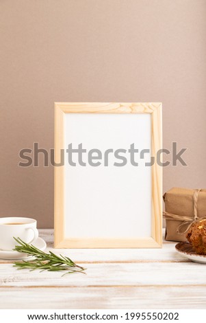 White wooden frame mockup with cup of coffee and cake on brown background. Blank, side view, still life.
