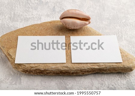 White paper business card, mockup with natural stone and seashell on gray concrete background. Blank, side view, still life, copy space.