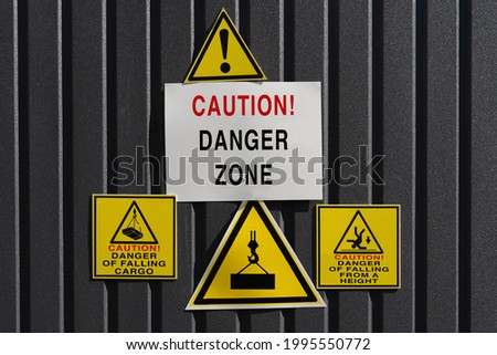 Metal Signs – Warning, Danger zone. Danger of falling cargo! Danger of falling from a height! triangle and square Warning Dangerous icons on a dark metal fence near the construction site
