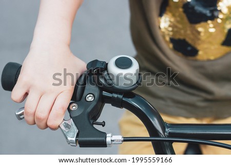 Child's hand on a bicycle handlebar. Bike bell. A child's hand holds a bicycle brake. Cycling trip. Bicycling. Braking. Royalty-Free Stock Photo #1995559166