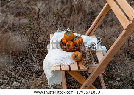 Sweet delicious persimmon, on a wooden stool, outdoors in the open air, against the background of an autumn landscape, beautiful colors, an interesting picture and seasonal orange fruits