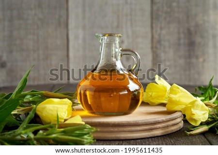 A bottle of evening primrose oil with fresh blooming Oenothera biennis plant on a rustic table. Alternative or herbal medicine.  Royalty-Free Stock Photo #1995611435