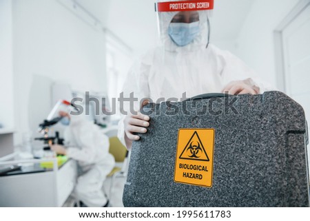 With biological hazard case. Female medical workers in protective uniform works on COVID-19 vaccine. Royalty-Free Stock Photo #1995611783