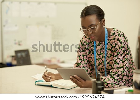 African female clothes designer working on a tablet in her studio Royalty-Free Stock Photo #1995624374