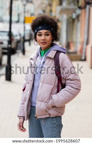 African american woman in jacket looking at camera on urban street