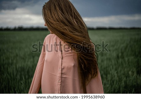 Long-Haired Woman In A Pink Dress On A Green Field  Before The Storm, Wind On Hair.