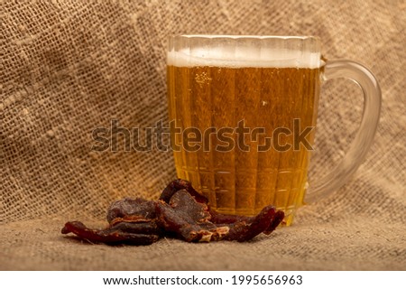 Pieces of dried caviar and a mug of beer on a table covered with a homespun cloth with a rough texture. Close-up, selective focus.
