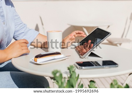 Close-up of a business woman's hand in a blue shirt working on a laptop in a cafe on a white table with a cup of coffee and cake. Selective focus