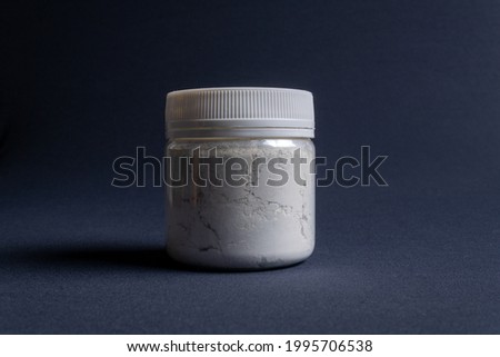 A pot containing resin of a white glitter color on a dark black background. Used for various purposes in industry and at home in the adaptation of furniture and objects for interior decoration.