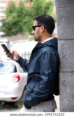 standing man looking at mobile leaning against a wall
