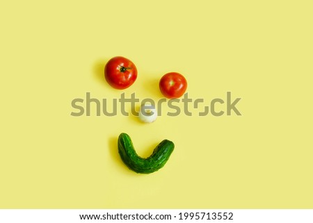Happy vegetables, vegetable face, tomato eyes, garlic nose, cucumber smile, top view, on a yellow background, copy space.