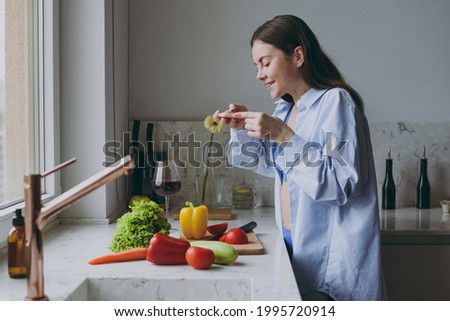 Young blogger housewife woman 20s in casual clothes blue shirt take photo of salad vegetables ingredients by mobile cell phone cook food in light kitchen at home alone Healthy diet lifestyle concept