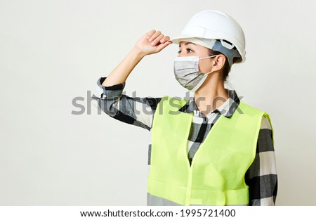 Worker woman wearing face mask and protective hard hat. Waist up portrait of young woman wearing hard hat on white background with copy space. Coronavirus Hygiene, safety concept
