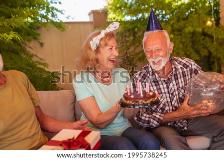 Group of cheerful senior friends having fun at a birthday party, host of the party holding a birthday cake after making a wish and blowing out candles