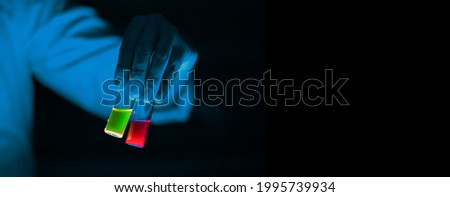 A woman scientist holding Organic chemistry sample glass vials in a laboratory - radioactive - fluorescence. A copy space black background. Organic medicinal chemistry laboratory.