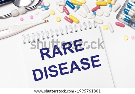 On a light background, multi-colored pills, a stethoscope, an electronic thermometer and a notebook with the text RARE DISEASE. Medical concept.