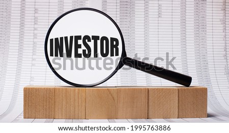 Against the background of reports on wooden cubes - a magnifying glass with the text INVESTOR. Business concept