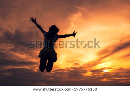 Silhouette successful young woman jumping outstretched hands in colorful sunset sky