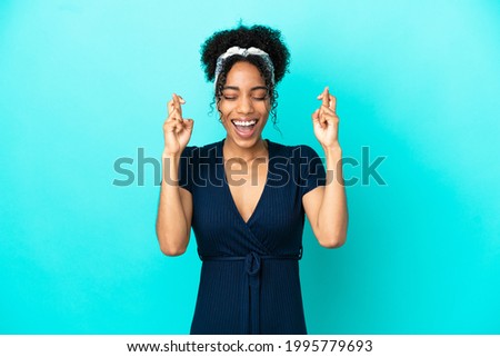 Young latin woman isolated on blue background with fingers crossing