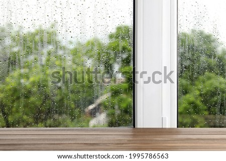 Empty wooden table near window on rainy day. Space for text Royalty-Free Stock Photo #1995786563