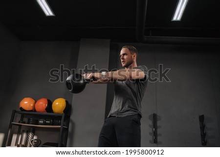 Strong muscular athlete doing kettlebell swings at crossfit gym, outfit shot on grey gym background with equipment. Weightlifter doing workout indoors, exercising. Crossfit instructor warming up Royalty-Free Stock Photo #1995800912