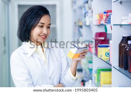 Asain female pharmacist holding and looking medicine packet in drugstore Thailand 
