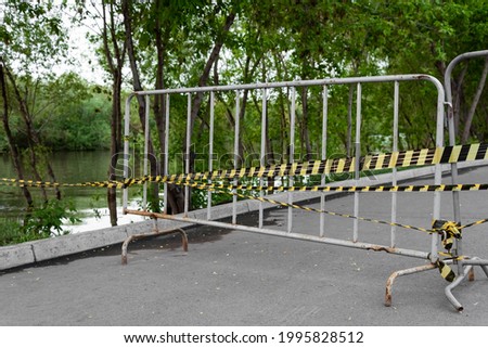 metal fence and yellow black safety tape green trees and river flood danger emergency 