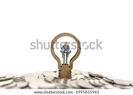 Business Financial and Idea Concept. Businessman miniature figure people sitting on wooden lightbulb icon on pile of coins cutout isolated white background.