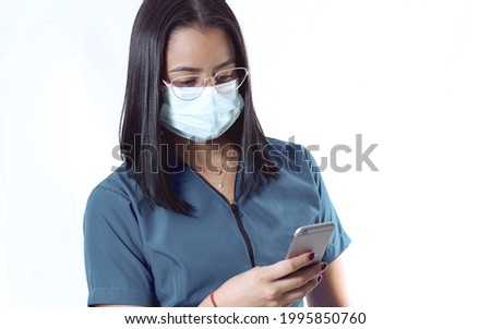 A young Hispanic doctor nurse wearing glasses and a sanitary mask using her phone