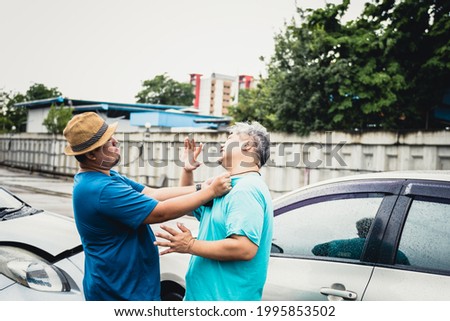 Two Asian middle-aged fat man are arguing, due to a accident car crash, while it was raining, to people and accident insurance concept. Royalty-Free Stock Photo #1995853502
