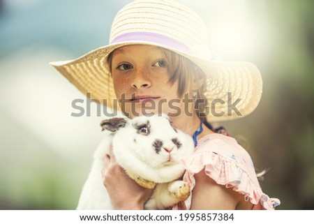 Young kid in a hat holding a scared rabbit in hands. Rabbit is scared to death probably.