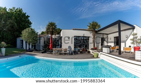 Trendy outdoor modern house, awning and patio roof, garden lounge, chairs, metal grill surrounded by landscaping