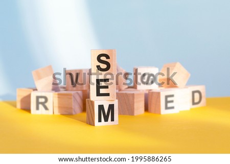 wooden cubes with letters sem arranged in a vertical pyramid, yellow background, reflection from the surface of the table, business concept. sem - short for search engine marketing