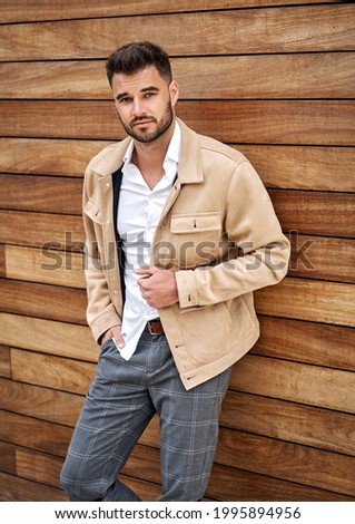 Handsome man in khaki jacket posing over wooden wall Royalty-Free Stock Photo #1995894956