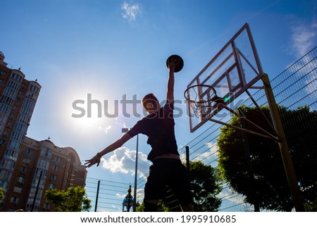 Silhouette of a man who throws a ball into a basketball hoop on the street against a sky with clouds in black and white color