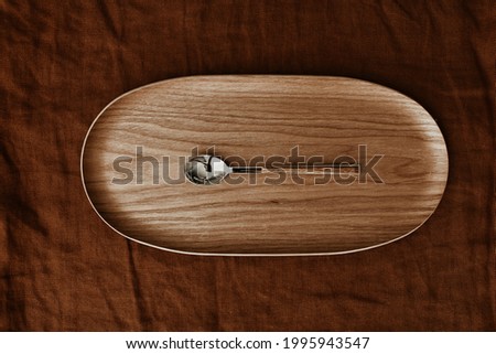 A metal spoon with wooden handle on a wooden tray on dark brown textile background. Flat lay, top view.